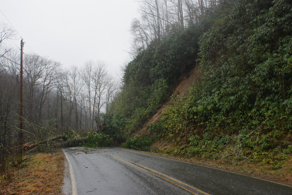 Photograph of a debris flow in western North Carolina showing brown debris flow material and its path of destruction, illustrating how slope failures mobilize into damaging flows